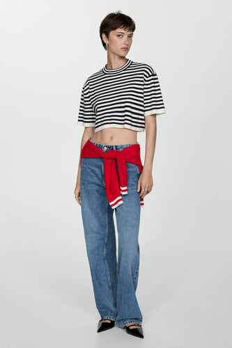 Vrouw in gestreepte crop top, blauwe jeans en rode trui, staand.