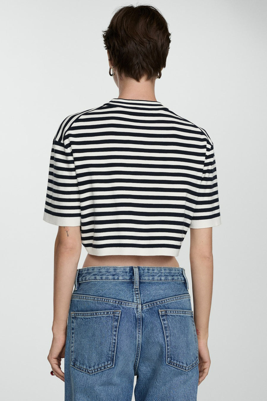 Achterkant van een vrouw met een gestreept crop-shirt en blauwe jeans.

