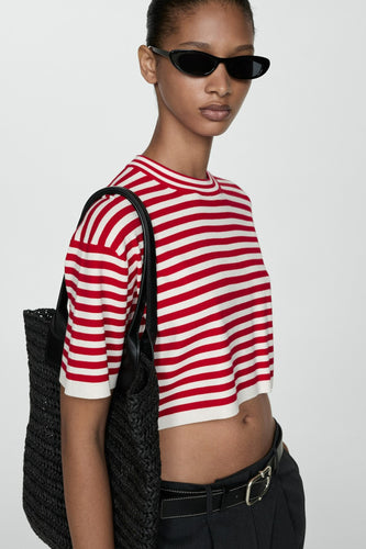 Model met gestreepte crop top, zonnebril en zwarte tas.