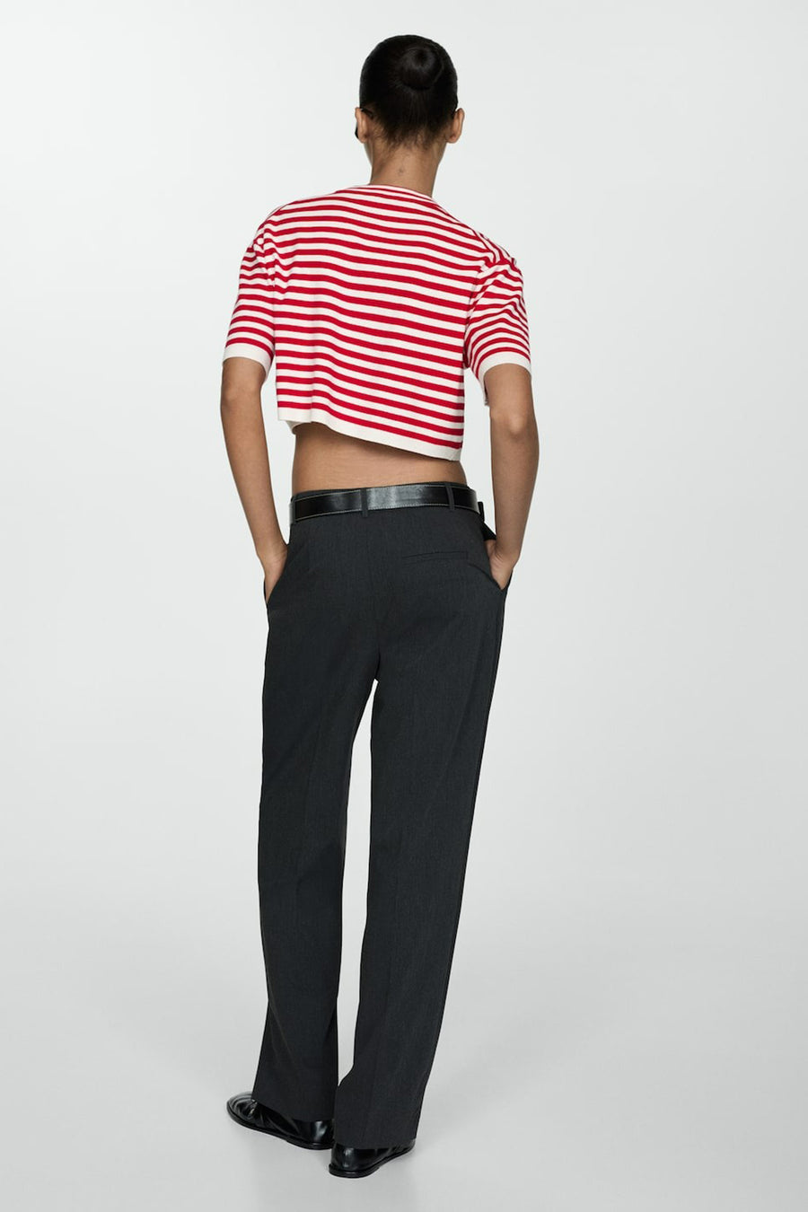 Vrouw in rood-wit gestreept shirt en zwarte pantalon met handen in zakken.
