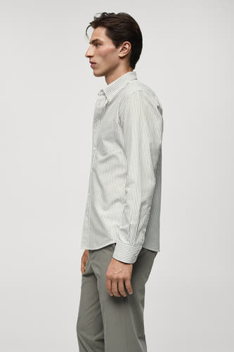 Chemise rayée verte avec longues manches de MANGO, montrée en profil latéral avec un pantalon gris.
