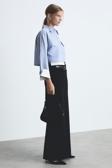 Chemise bleue à manches longues de MANGO, portée avec un pantalon noir et une petite poche noire.