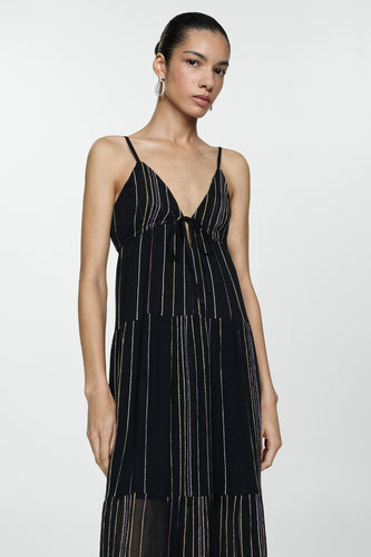 Een vrouw in een mouwloze, zwarte jurk met gekleurde strepen.