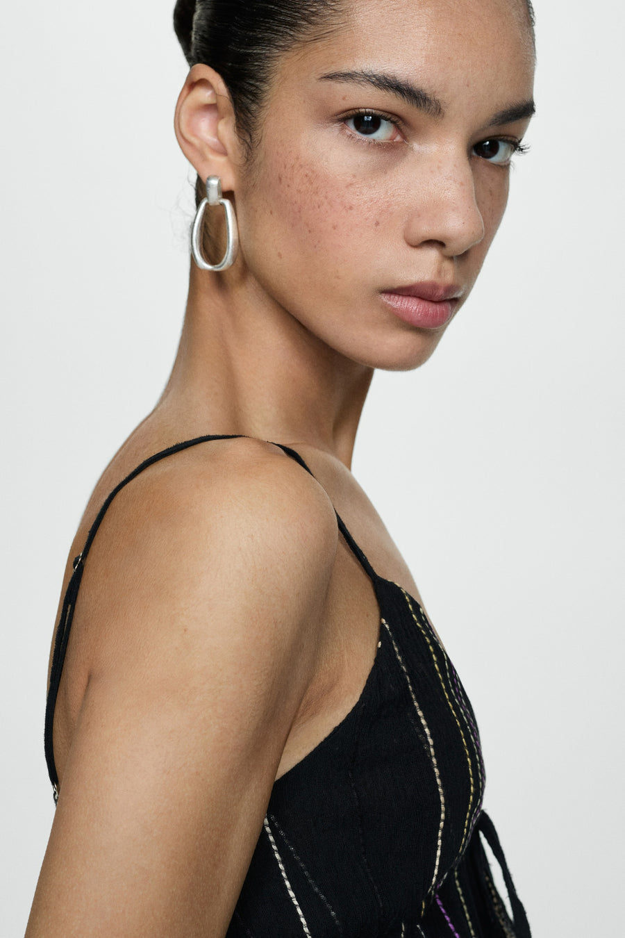 Portret van vrouw met zwarte top en zilveren oorbel tegen witte achtergrond.