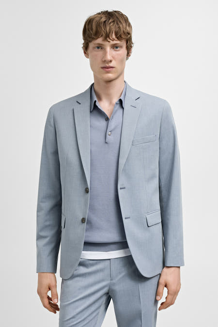 Blazer bleu de MANGO, visible sur le côté, associé à un pantalon coordonné et des chaussures noires.