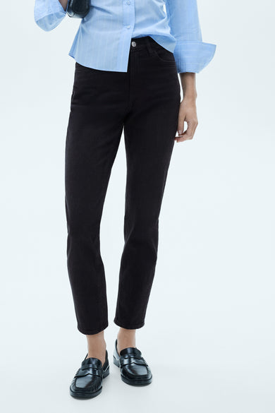 Jean mom noir de MANGO, associé à une chemise rayée bleu clair et des baskets noires.