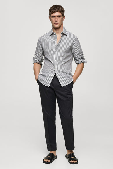 Chemise rayée gris clair et foncé avec longues manches de MANGO, portée avec un pantalon noir et des sandales.
