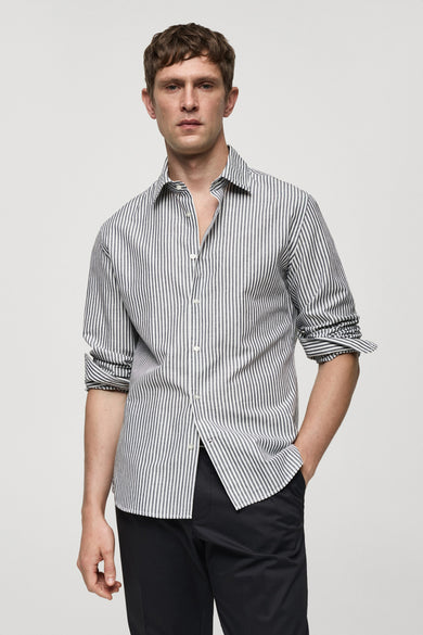 Chemise rayée grise de MANGO à manches longues, avec des manches retroussées et portée avec un pantalon noir.