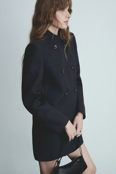 Manteau bleu de MANGO, à double boutonnage avec des boutons, porté avec une poche main noire.