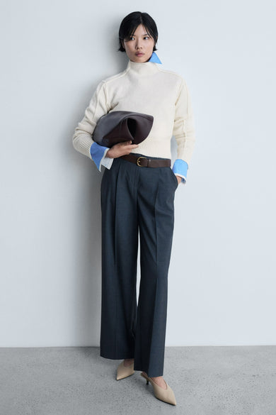 Pull-over blanc avec col rond de MANGO, porté avec un chemisier bleu et un pantalon gris foncé à plis.
