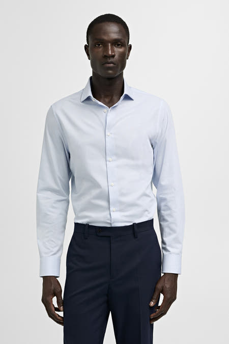 Blauw overhemd met lange mouwen van MANGO, effen design met subtiele streeptextuur, gecombineerd met donkerblauwe pantalon.
