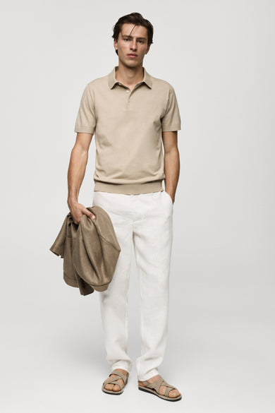 Polo beige à manches courtes de MANGO, tissu lisse, coupe classique, modèle en pose lifestyle avec pantalon blanc et sandales