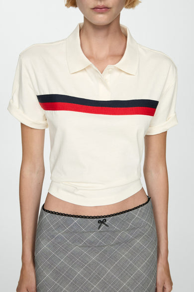 Polo blanc à manches courtes de MANGO, avec une rayure rouge et noire, porté avec un mini-jupe.