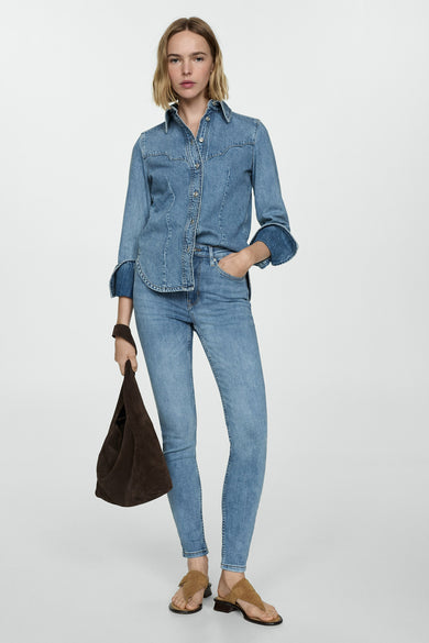 Jean skinny en denim bleu moyen de MANGO, avec un t-shirt en denim à manches longues et une sac marron.