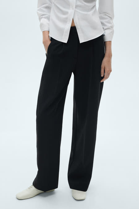 Pantalon noir de MANGO, vu de l'rière avec une longue et large et et des chaussures plates assorties.