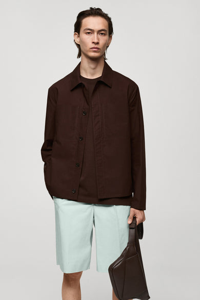 Manteau court rouge de MANGO, vu de derrière, avec des short bleus et un sac marron.
