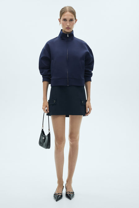 Gilet bleu de MANGO, porté avec une jupe coordonnée à poches et des escarpins noirs à lacets.