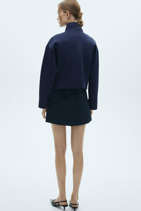 Blauwe gilet van MANGO, achterkant gezien, gecombineerd met een minirok en puntige slingbacks.