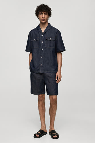 Jean en denim court bleu marine de MANGO, avec un chemisier en denim coordonné et des sandales noires.