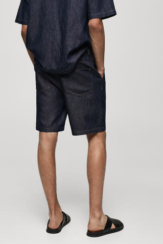 Shorts en denim bleu moyen de MANGO, dos, associé à une chemise en denim et des sandales noires.