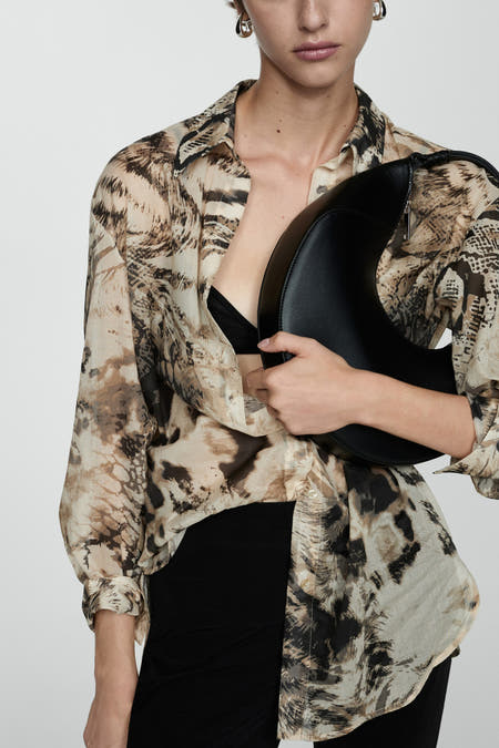 Blouse beige à longues manches de MANGO, avec un imprimé animal et portée avec un soutien-gorge noir et une jupe.