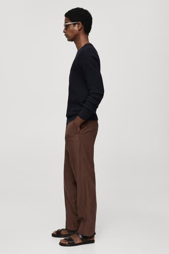 T-shirt bleu avec col rond de MANGO, à rayures et associé à un pantalon marron et des sandales noires, vue latérale.