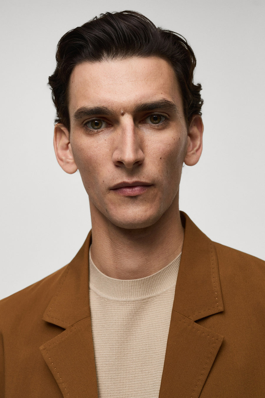 Oranje blazer van MANGO, gedragen over een crèmekleurige top met een subtiele textuur, in een close-up vooraanzicht.
