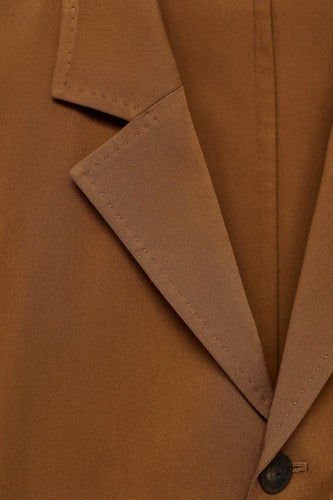 Oranje blazer van MANGO, met een reverskraag en een enkele knoopsluiting, close-up.
