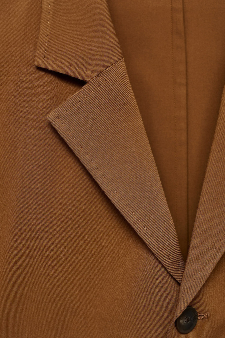 Oranje blazer van MANGO, met een reverskraag en een enkele knoopsluiting, close-up.
