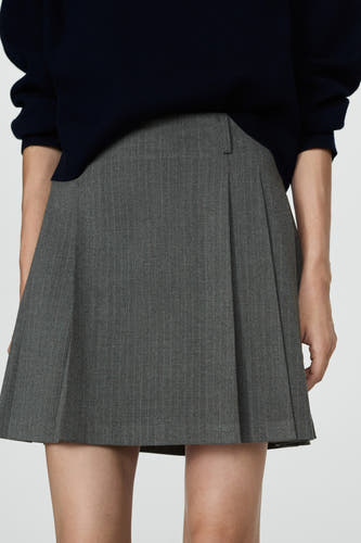 Jupe grise courte de MANGO avec une rayure et des plis, portée avec un pull bleu foncé.