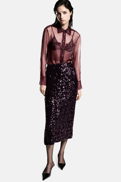 Robe rouge de MANGO avec paillettes, associée à une blouse transparente, un soutien-gorge noir et des escarpins.