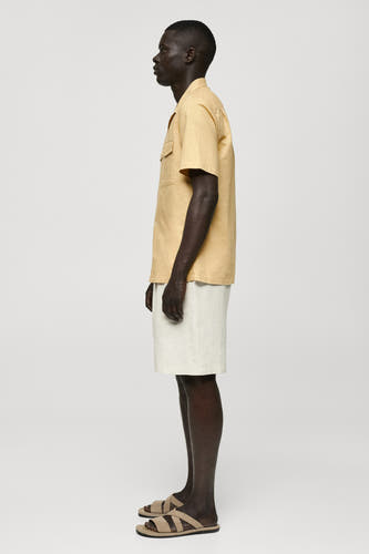 Geel, kort mouwen hemd van MANGO, in zijaanzicht, met witte shorts en sandalen.
