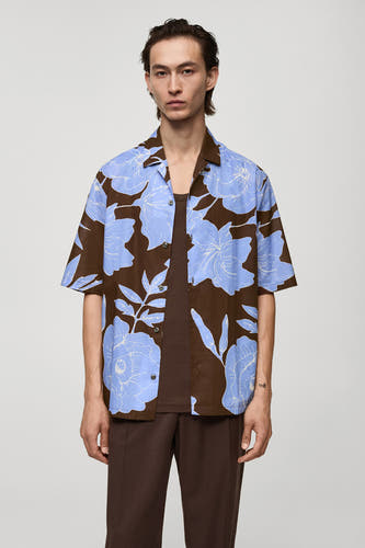 T-shirt à fleurs brun avec manches courtes de MANGO, avec des motifs floraux bleus, associé à un tank-top brun et un pantalon.