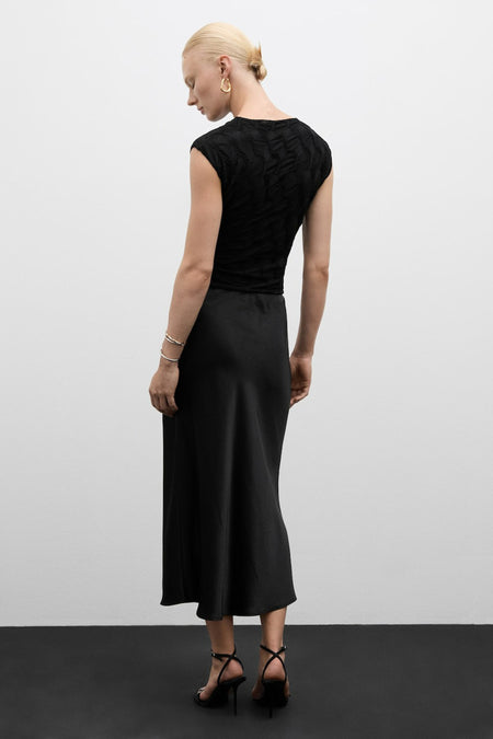 Blouse noire à manches courtes avec texture de MANGO, vue de dos, portée avec une jupe noire et des talons