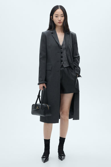Shorts multicolores de MANGO, associés à une veste grise, un blazer et un manteau long, des chaussettes noires et des chaussures, avec une sacoche noire.