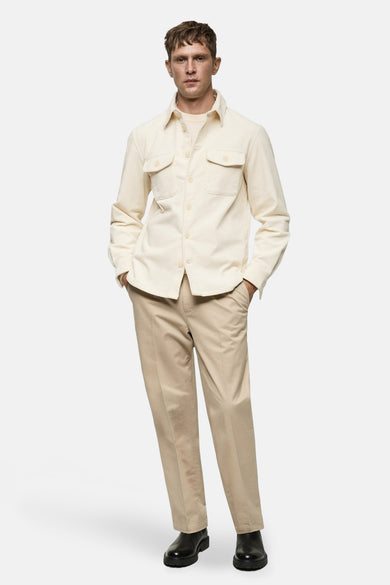 Blouse blanche à manches longues de MANGO, avec poches poitrine et portée avec un pantalon beige et des chaussures noires.