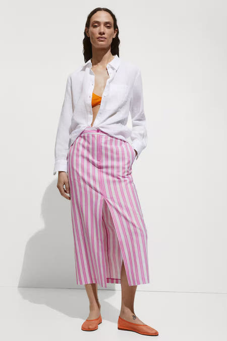 Long jupe rayée rose de MANGO, avec une fente à l'avant, associée à un chemisier blanc et des chaussures orange.