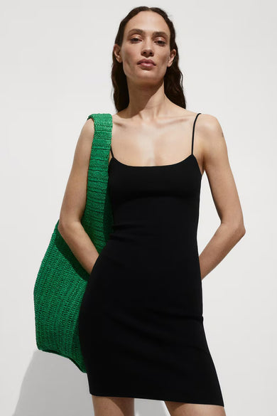 Robe sans manches noire de MANGO, portée par un modèle aux cheveux ondulés foncés, gros plan du visage, du cou et des épaules.