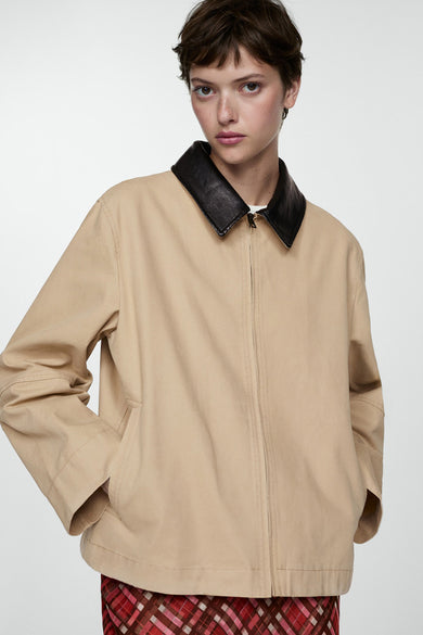 Manteau court blanc de MANGO, avec des manches longues et un col noir, associé à une jupe plissée.