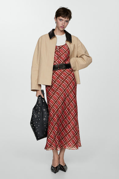 Manteau court blanc de MANGO, avec une collier cuir noir, porté sur une robe rouge à carreaux et une ceinture noire.