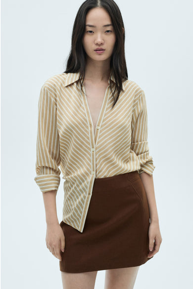 Jupe brune courte de MANGO, associée à un chemisier rayé à longues manches dans un style décontracté.