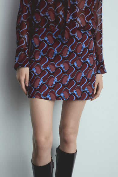 Short red skirt from MANGO with wavy blue pattern and worn with black boots.