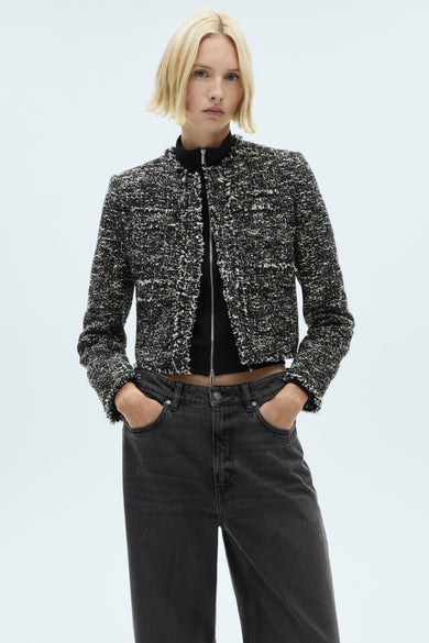 Blazer multicolore de MANGO, avec une texture tweed et des manches longues, porté avec un haut noir et des jeans foncés.