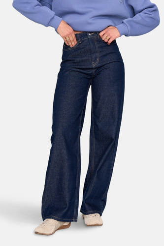 Jean denim bleu marine avec des jambes larges de 24 Colours GMBH, associés à des chaussures beige et une chemise bleue.
