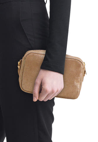 Sac à bandoulière taupe Access® avec effet pailleté et quincaillerie dorée, tenu par une personne vêtue de noir.