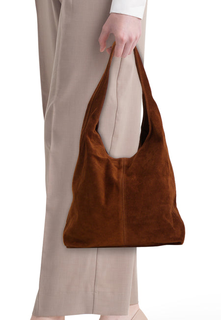 Sac à bandoulière hobo en suède marron Access® avec surpiqûres décoratives, porté avec un pantalon beige.