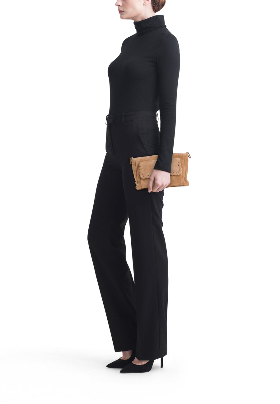 Sac à bandoulière beige Access® en daim avec surpiqûres décoratives et fermeture à rabat, porté par une femme en tenue noire.