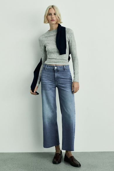 Jean bleu marine large de MANGO, associé à une chemise grise et des chaussures marron.