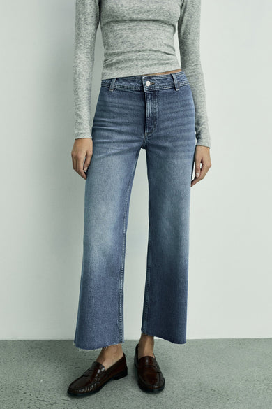 Jean bleu marine large de MANGO, avec des bords finis et une longue chemise grise.