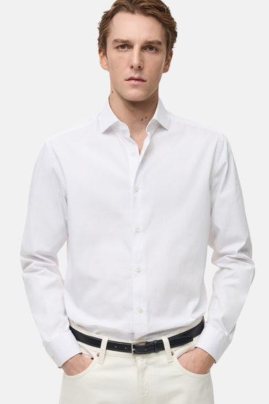 Blouse blanche à manches longues de MANGO, avec des rayures verticales subtiles, portée avec une ceinture noire et un pantalon crème.